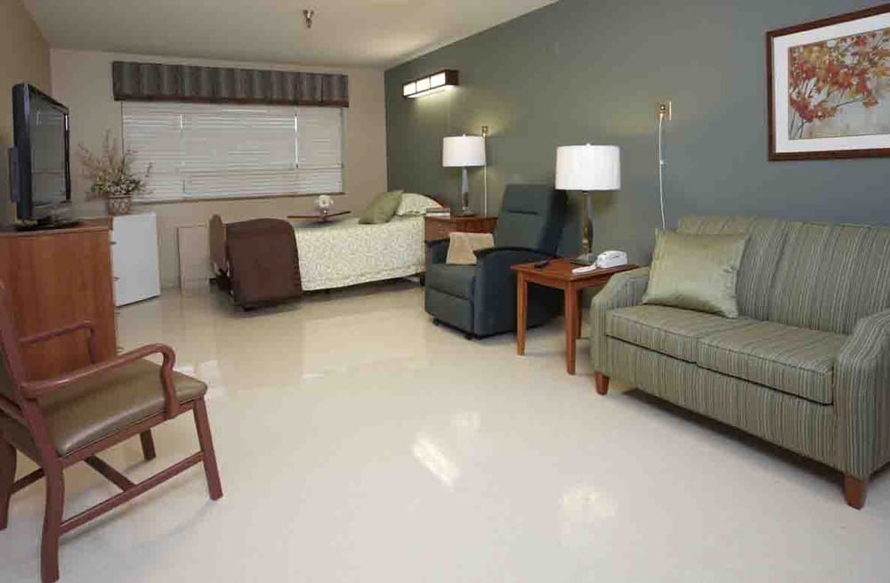 A hospital room with a bed, chairs, and lamps.