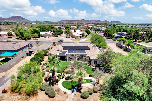 A serene aerial view of a suburban home featuring solar panels and lush landscaping.