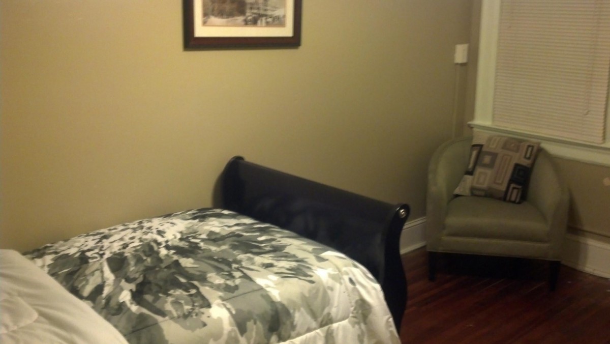A cozy bedroom with a bed and chair, featuring wall art.