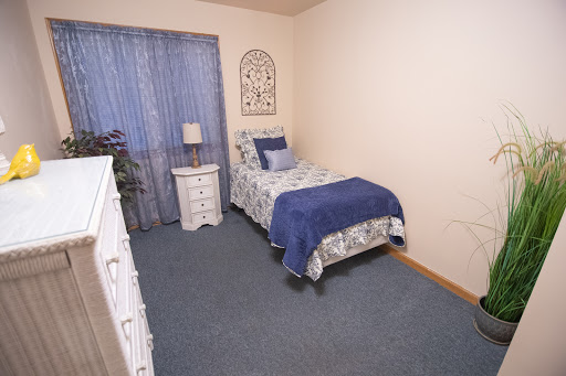 A cozy bedroom featuring a single bed adorned with blue bedding, complemented by a nightstand and curtains.