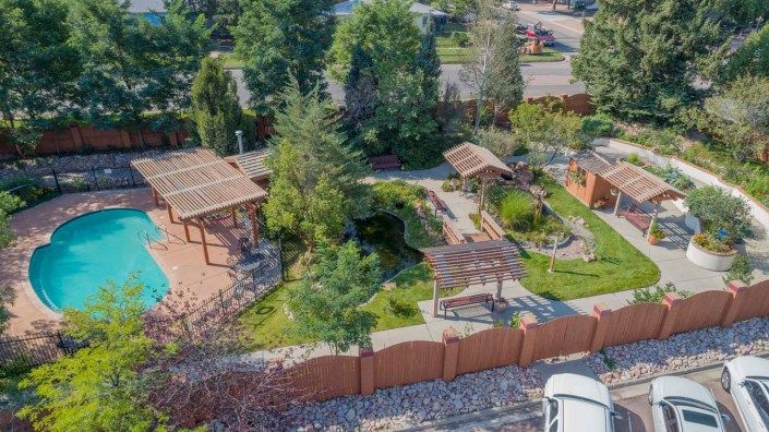 Aerial view of a beautifully landscaped garden featuring pergolas, lush greenery, and well-maintained outdoor spaces surrounded by a decorative fence.