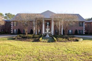 A large brick house with white columns, surrounded by landscaped gardens and a well-maintained lawn.
