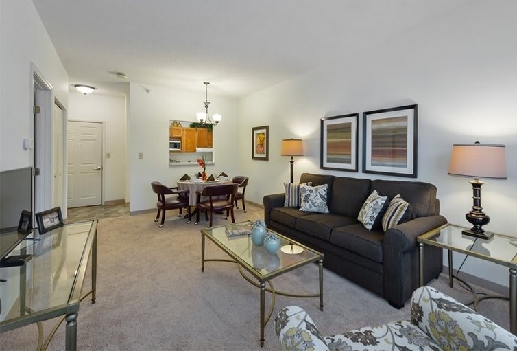 A cozy living room with a sofa, coffee table, dining area, and decorative artwork on the walls.