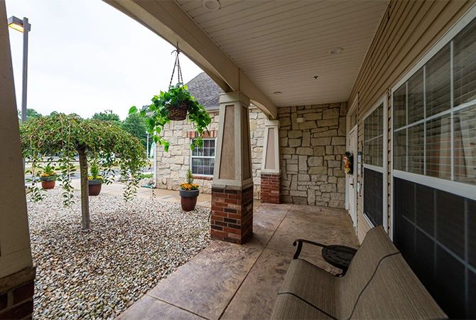 A cozy covered porch with stone walls, outdoor seating, and lush greenery.