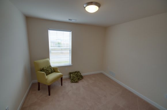 A minimalist empty room with a single chair and cushions near a window.