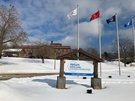 A snowy landscape featuring a building with three flags and a sign for Atrium Health's Carolinas Rehabilitation.