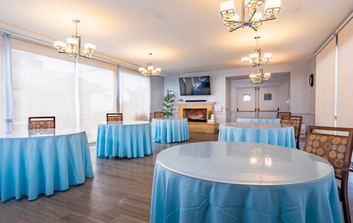 A well-decorated event room with round tables covered in blue tablecloths and elegant chandeliers.