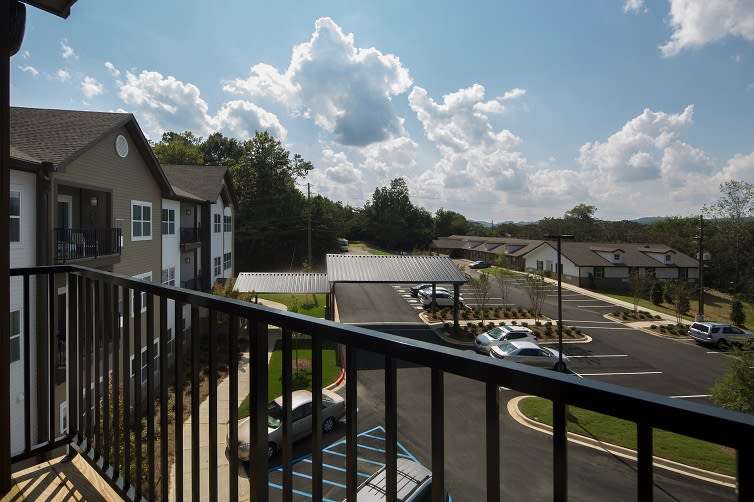 View from a balcony overlooking a parking lot in a residential area with a cloudy sky.