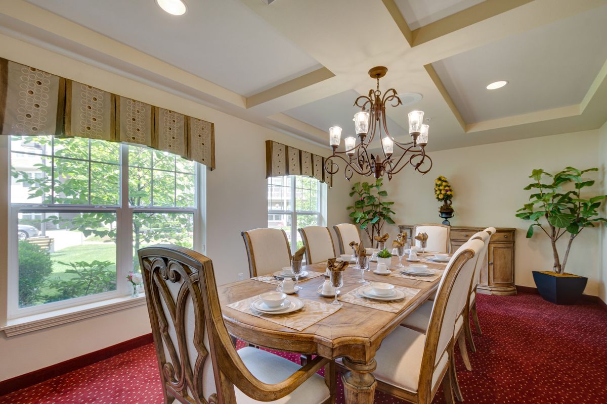 An elegant dining room featuring a large wooden table set for a meal, illuminated by a chandelier and surrounded by large windows.