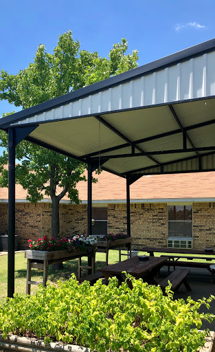 A sunny outdoor pavilion providing shade for a picnic area, surrounded by lush greenery.