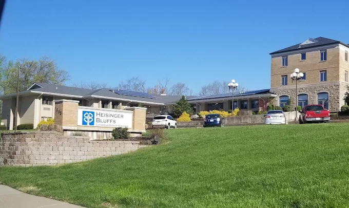 A school building with a sign and cars parked in front on a clear day.