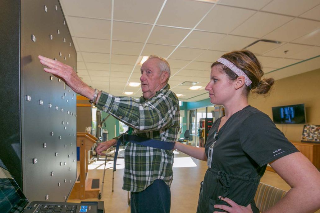 An elderly man participates in a physical therapy session with assistance from a therapist.