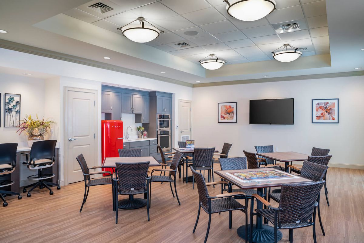 A modern dining area with a kitchenette, featuring a red refrigerator and multiple tables and chairs.