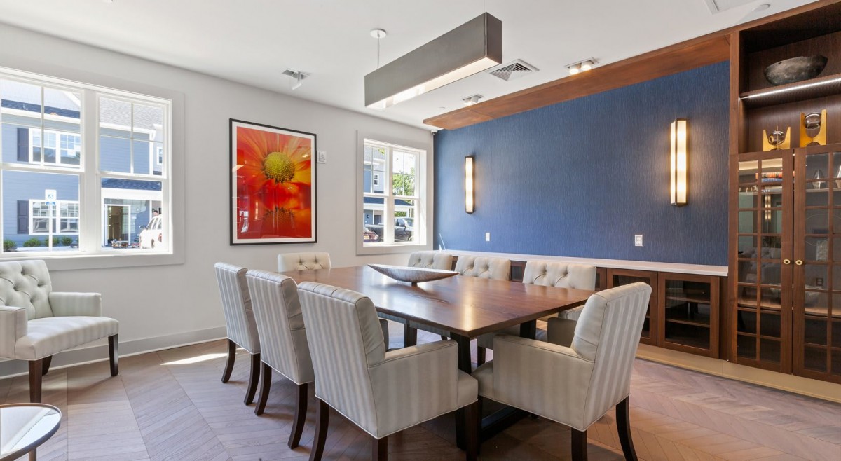 A modern dining room with a large table, upholstered chairs, and colorful artwork on the wall.