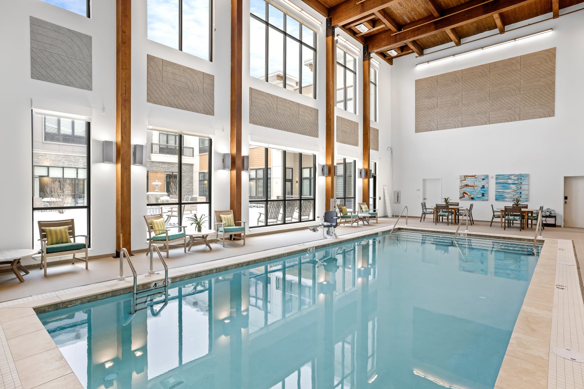 A modern indoor swimming pool area with large windows and wooden beams.