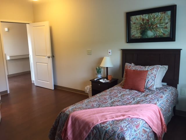 A cozy bedroom featuring a single bed with colorful bedding, a bedside lamp, and artwork on the wall.