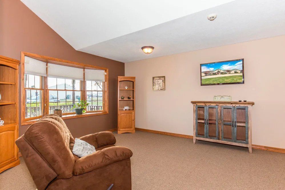 A cozy living room with a brown armchair, a large window, and decorative elements including a cabinet and a painting.