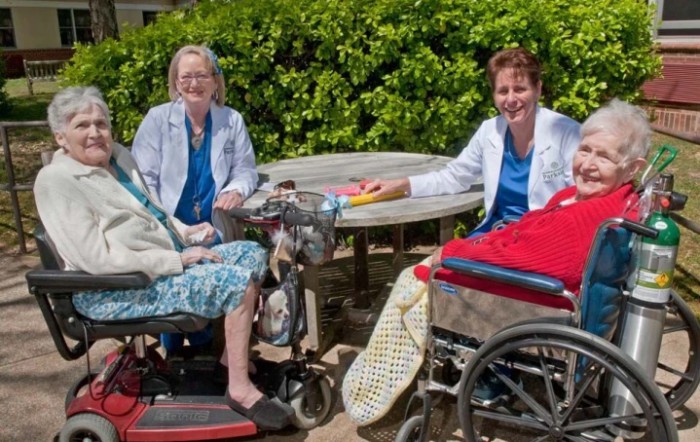 A group of elderly individuals and caregivers enjoying time outdoors in a park setting.