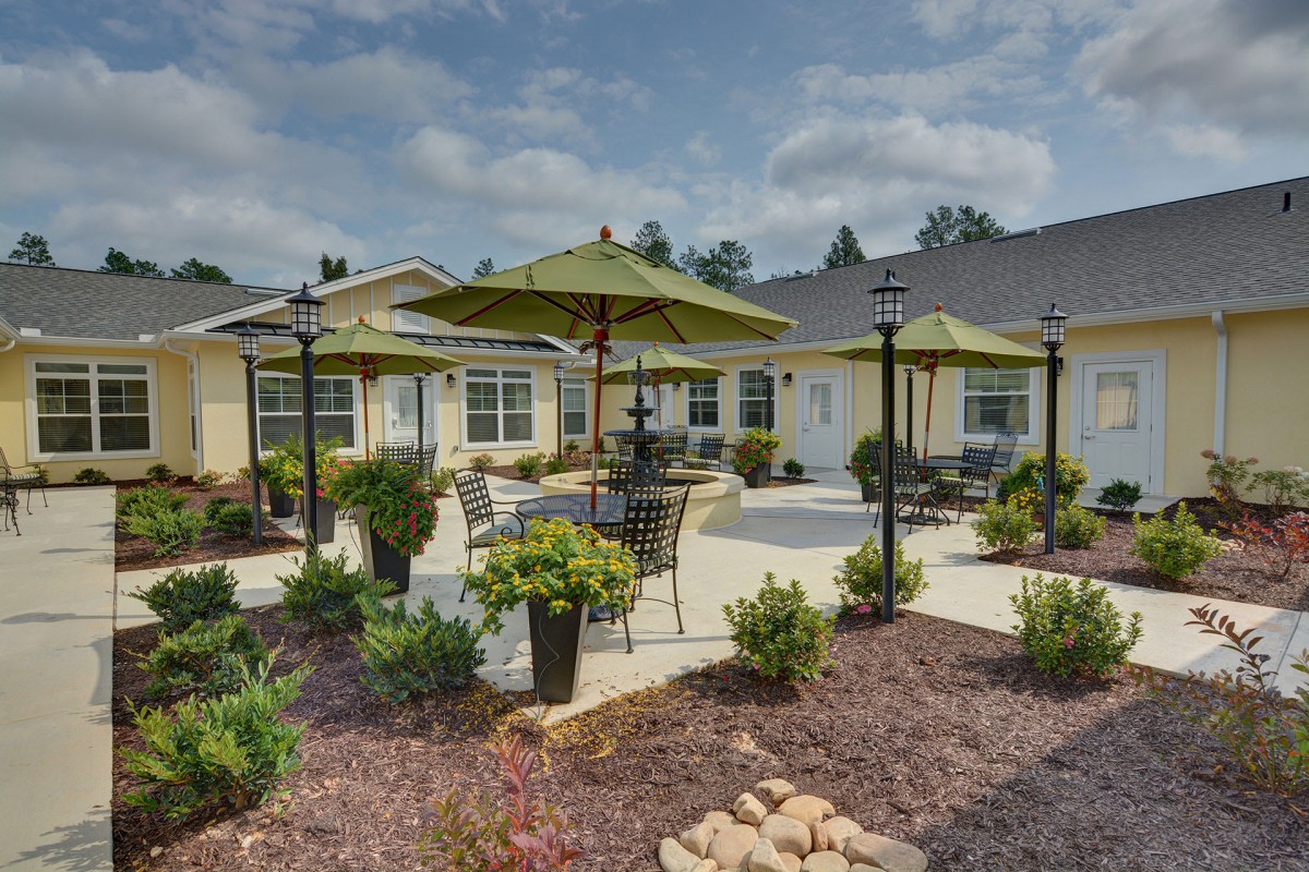 A sunny patio with outdoor seating and umbrellas surrounded by landscaping.