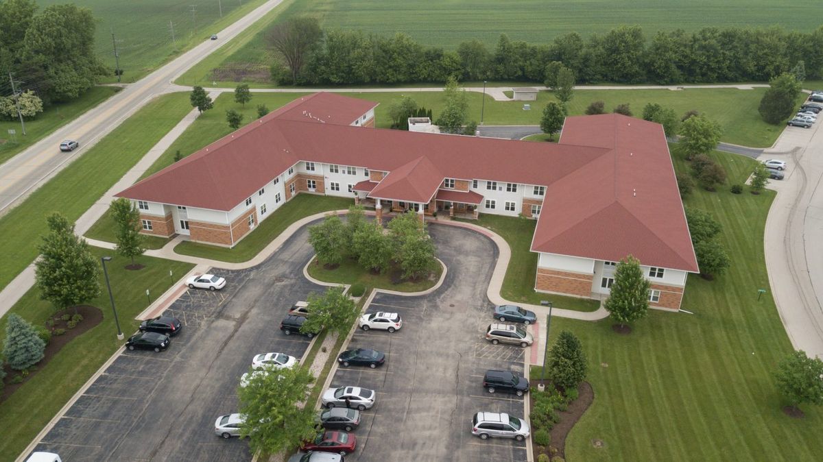 An aerial view of a large building with a red roof, surrounded by a parking lot and greenery.