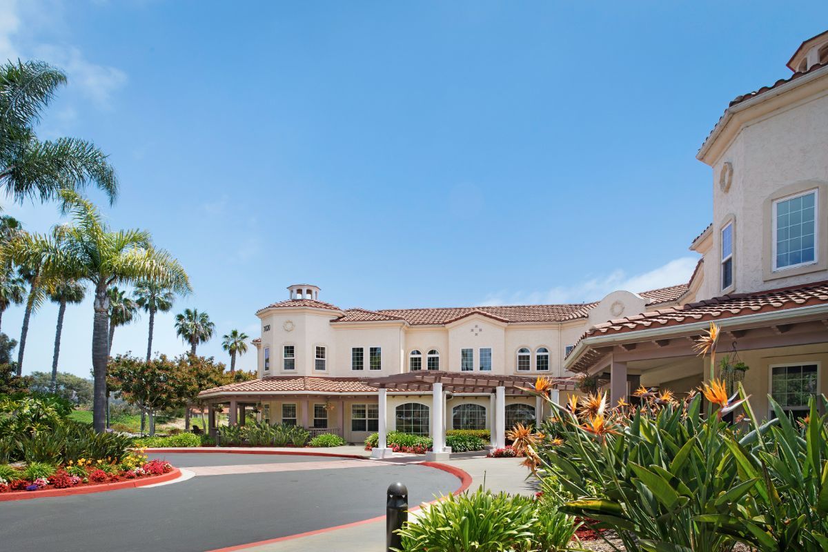 A sunny view of a large building with palm trees and landscaped grounds.