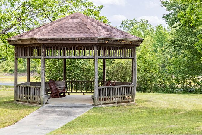 A wooden gazebo situated in a park surrounded by greenery and trees.