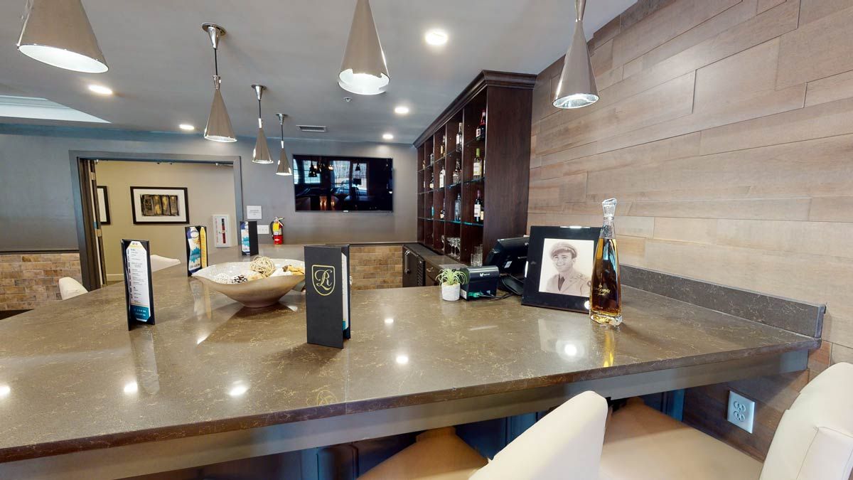 A modern bar setup with a sleek countertop, hanging lights, and a collection of bottles.
