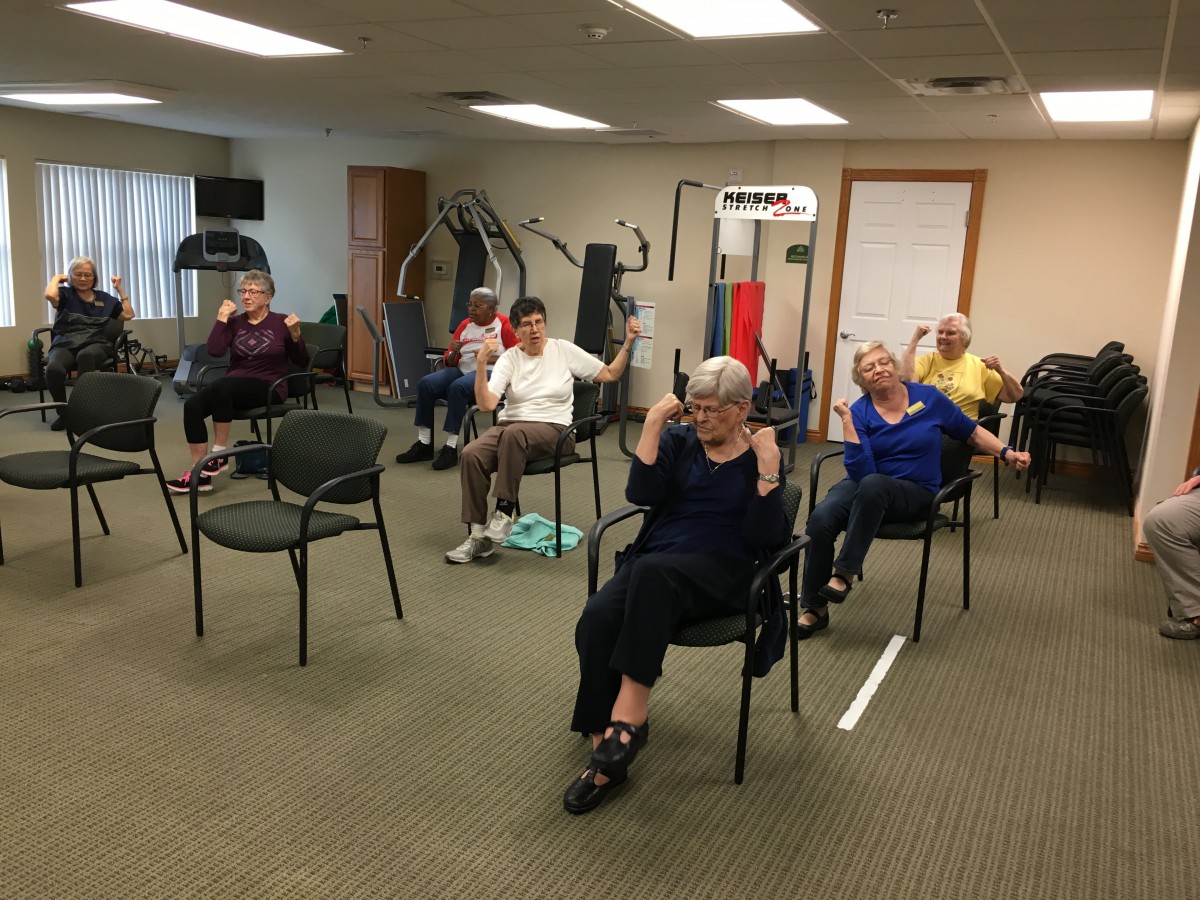 A group of seniors participating in a chair exercise class indoors.