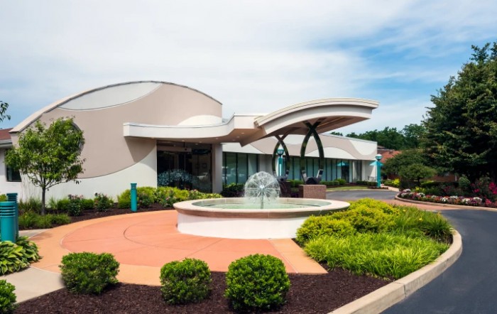 A modern building with a unique curved architecture and a fountain in the foreground, surrounded by landscaped greenery.