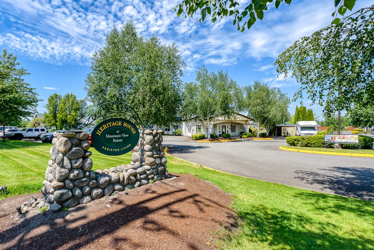 Entrance with a stone wall and sign, surrounded by trees and a driveway.