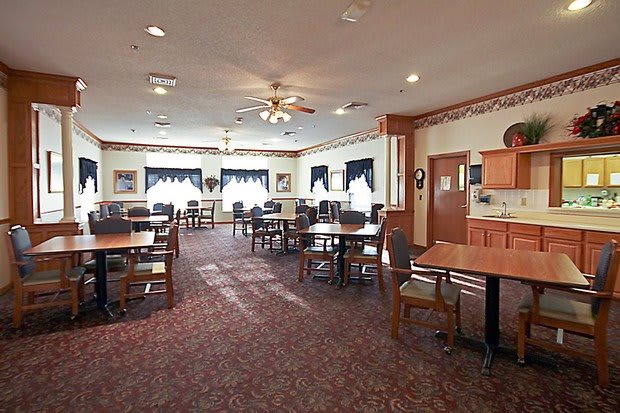 A well-lit dining area featuring multiple tables and chairs with a carpeted floor.