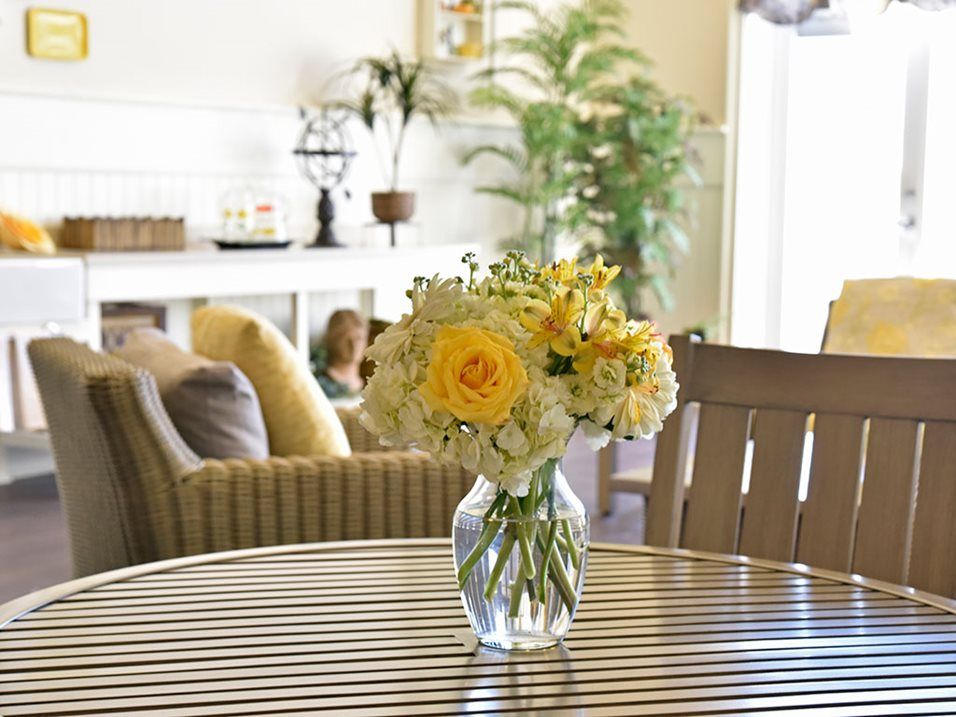 A vase with yellow and white flowers on a wooden table in a cozy living room setting.