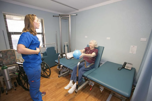 A healthcare professional assists an elderly patient with a therapeutic exercise in a rehabilitation setting.