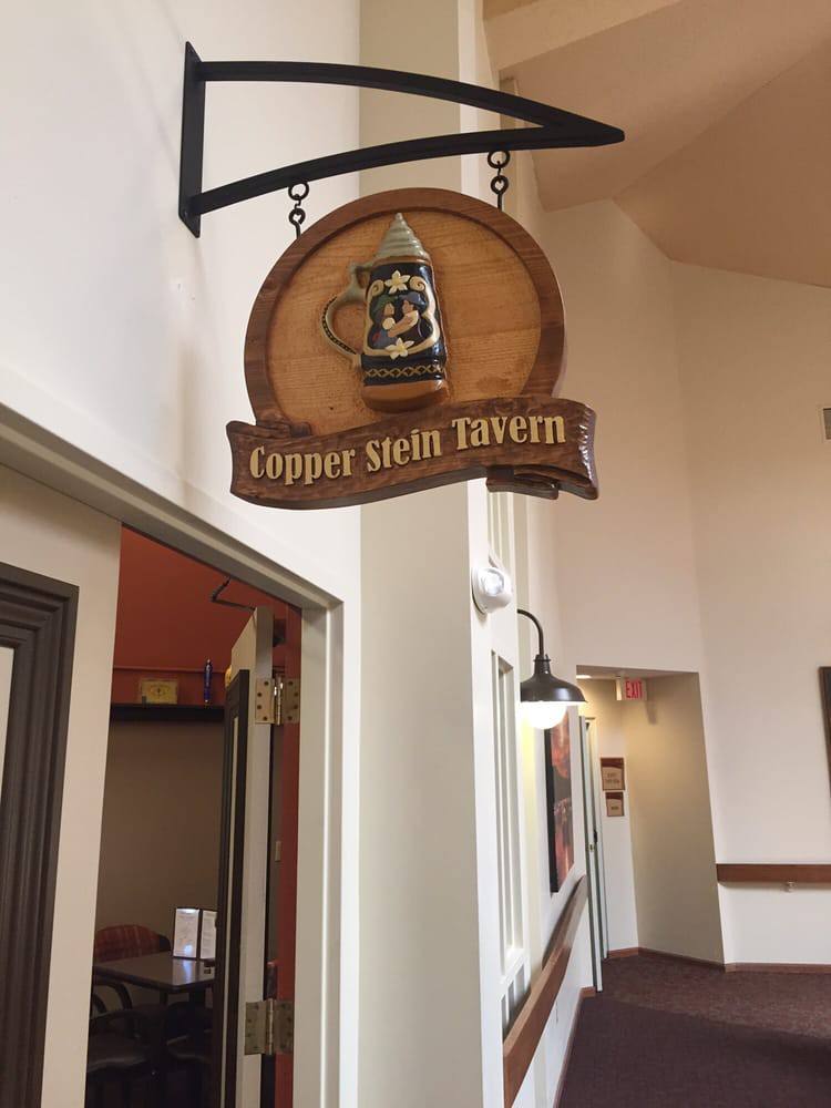 A wooden sign for the Copper Stein Tavern hanging indoors.