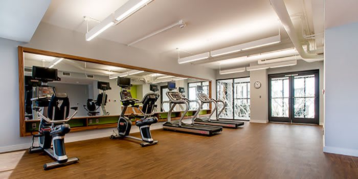 A modern gym room featuring treadmills and stationary bikes with large mirrors on the walls.