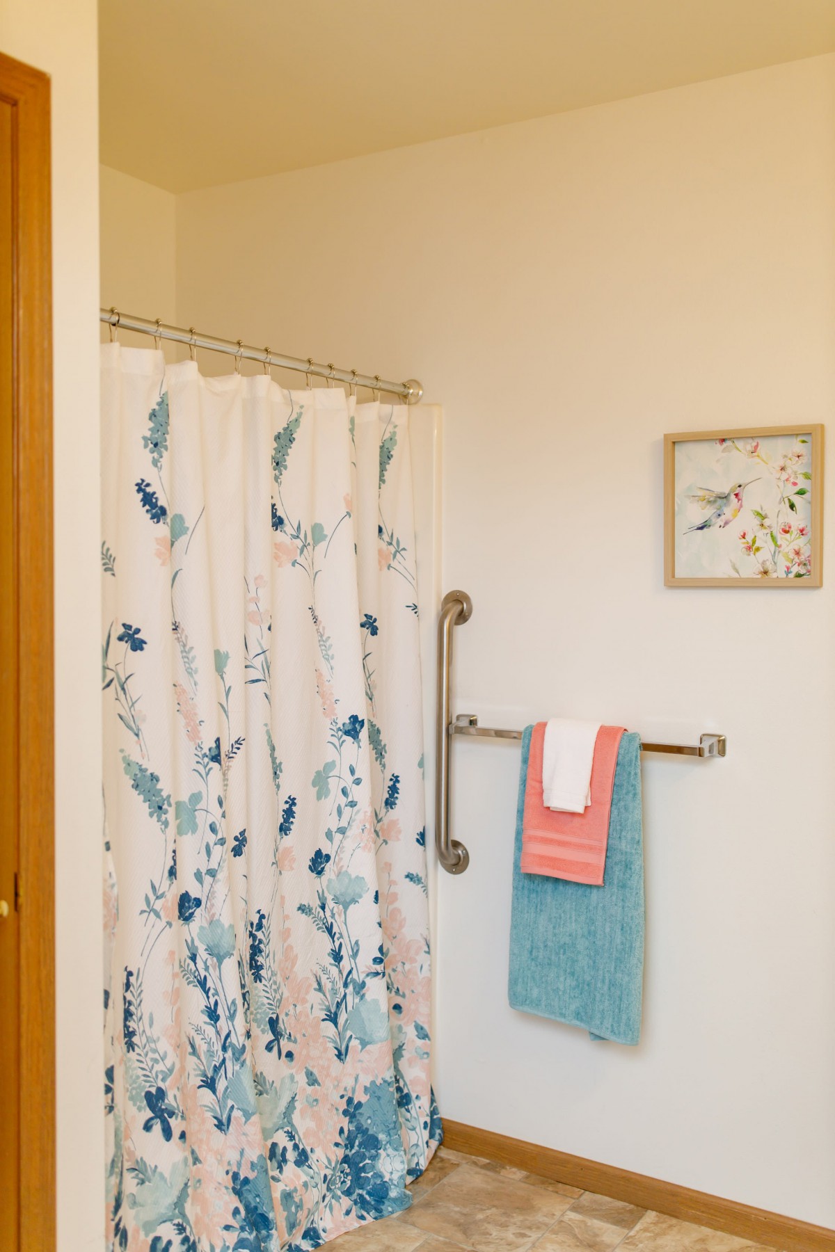A bathroom with a floral shower curtain, neatly hung towels, and a decorative wall piece.