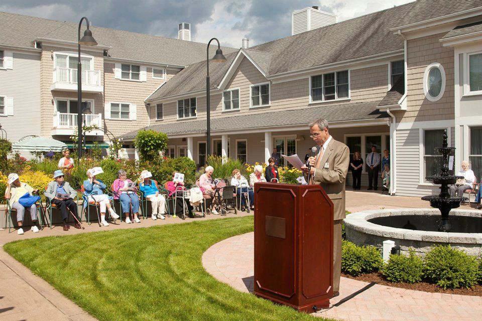 A speaker addresses an audience seated outdoors in front of a building.