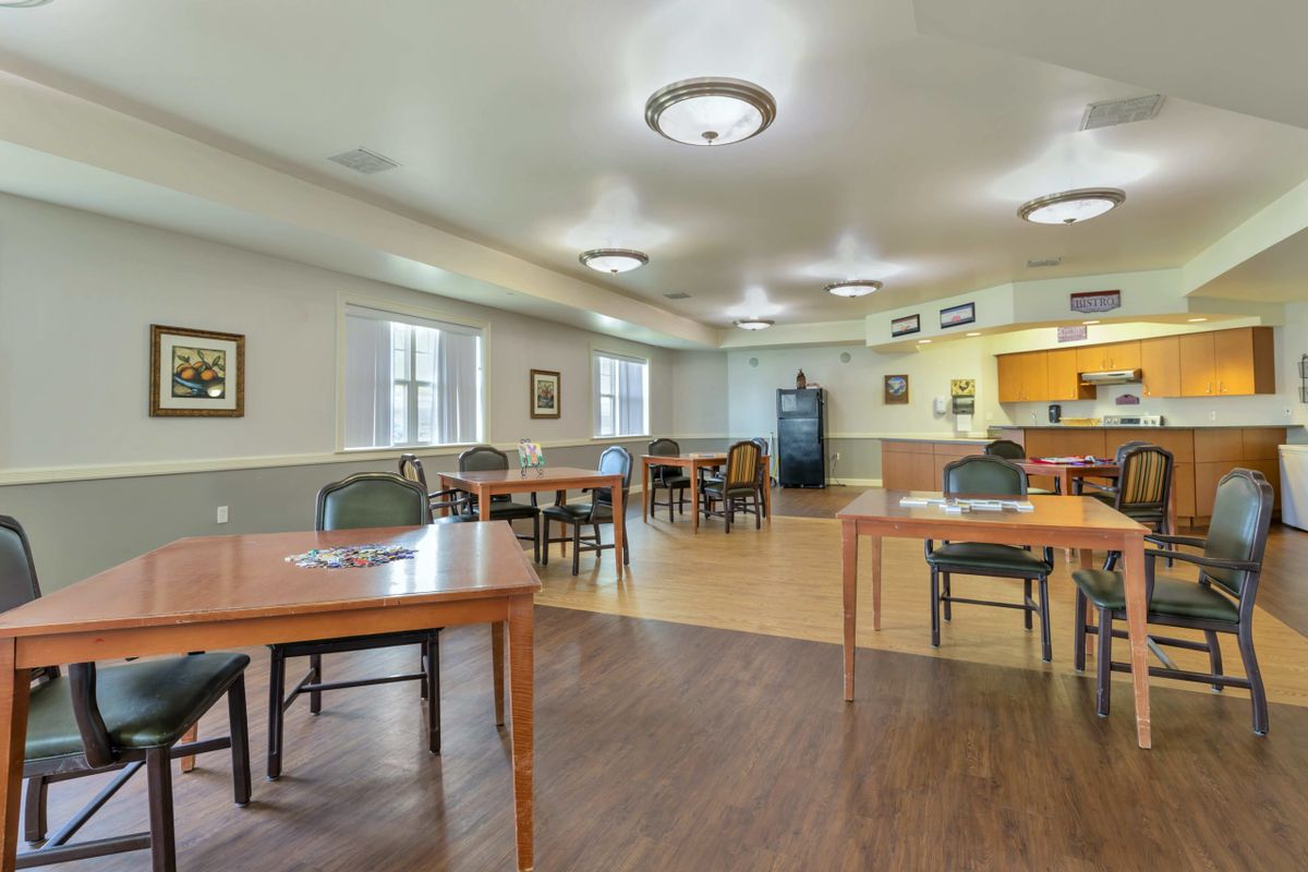 A community dining area with tables and chairs, featuring a wooden floor and modern lighting.