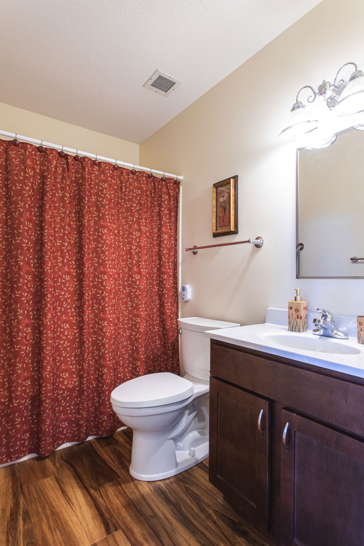 A clean bathroom with a red shower curtain and dark wood vanity.