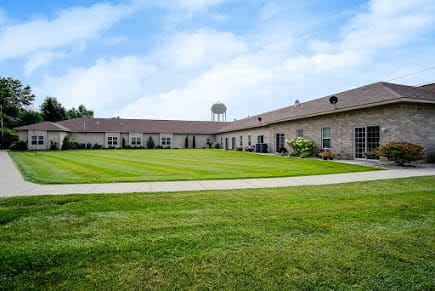 A wide view of a building complex surrounded by a well-maintained grassy area under a cloudy blue sky.