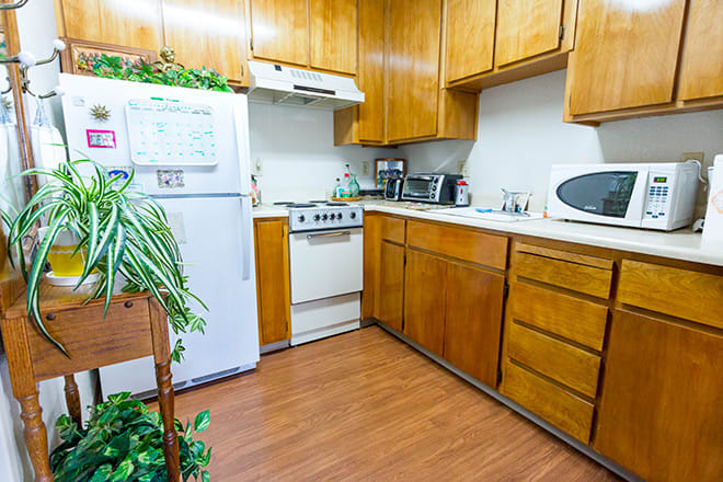 A cozy kitchen featuring wooden cabinets, a stove, and a refrigerator, with plants adding a touch of greenery.