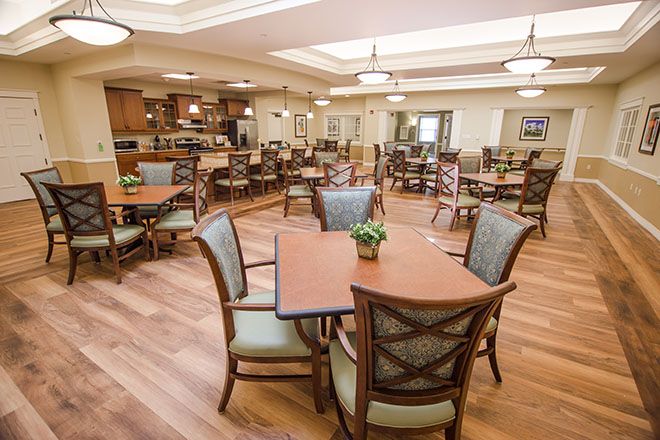 A spacious dining area with neatly arranged tables and chairs, featuring warm lighting and wooden flooring.