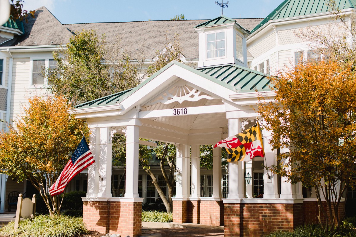A colonial-style building entrance with American and state flags surrounded by autumn trees.