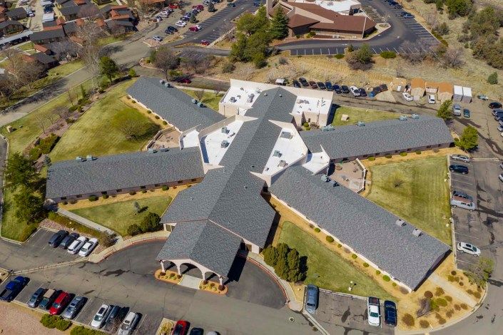 Aerial view of a cross-shaped building with surrounding landscapes and parking lots.