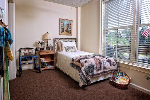 A cozy and well-lit bedroom featuring a single bed, nightstand with a lamp, and decorative items.
