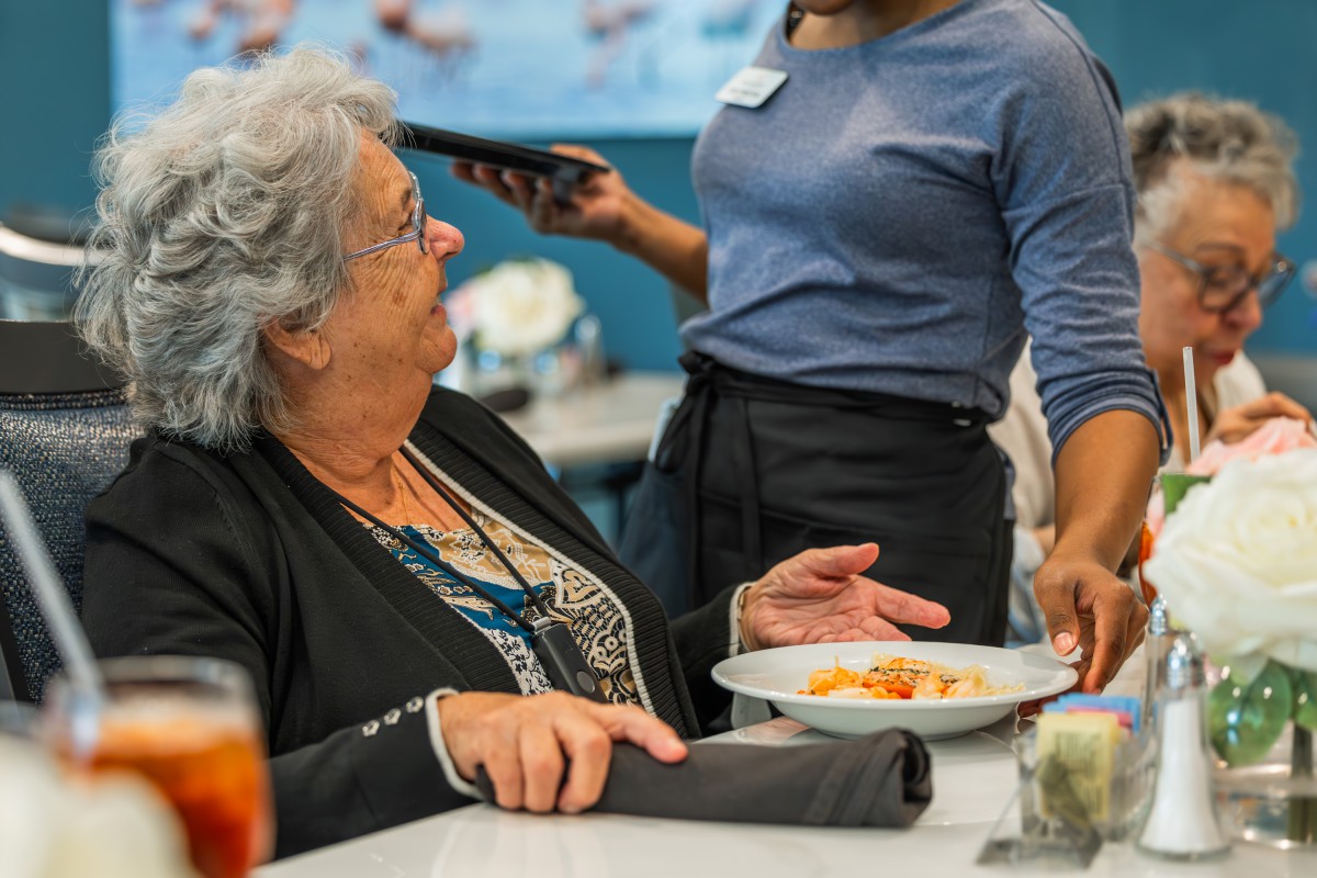 An older woman is being served a meal by a waitress in a restaurant setting.
