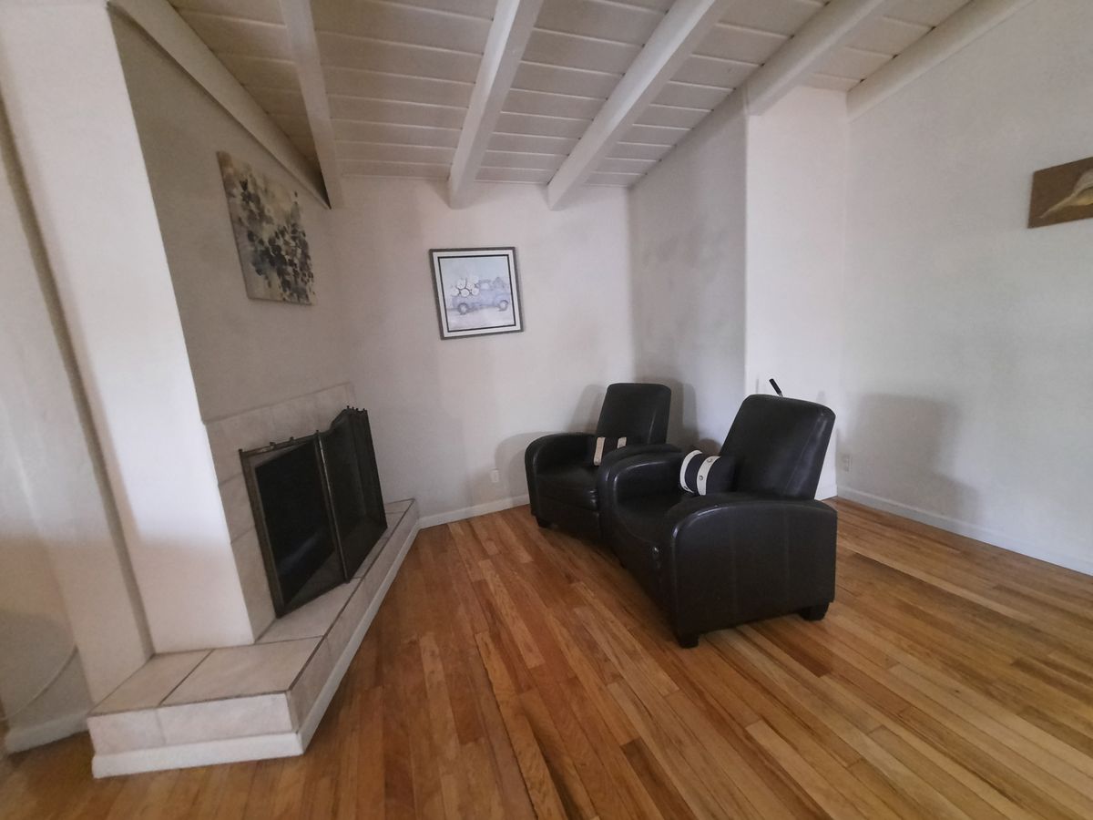 A cozy living room features two black leather chairs facing a fireplace, with artwork on the walls and a wooden floor.
