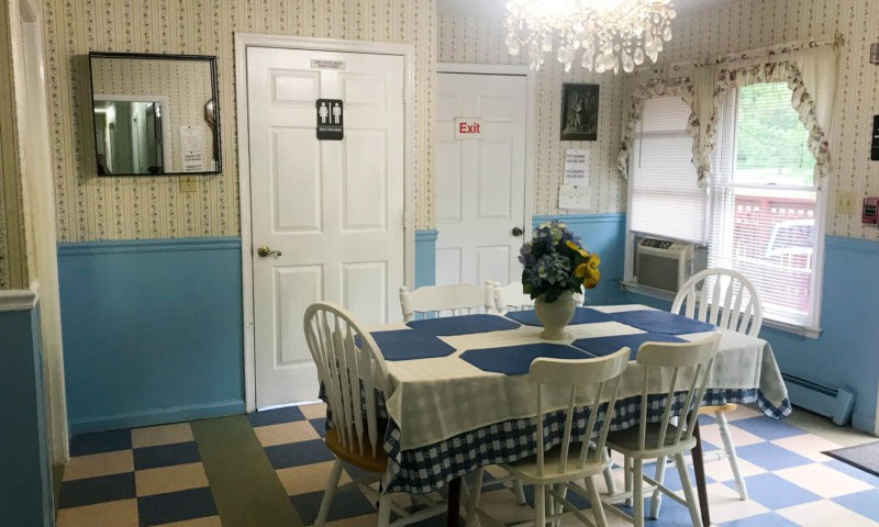 A charming dining room with blue and white decor, featuring a table set with a floral centerpiece, surrounded by chairs and illuminated by a chandelier.