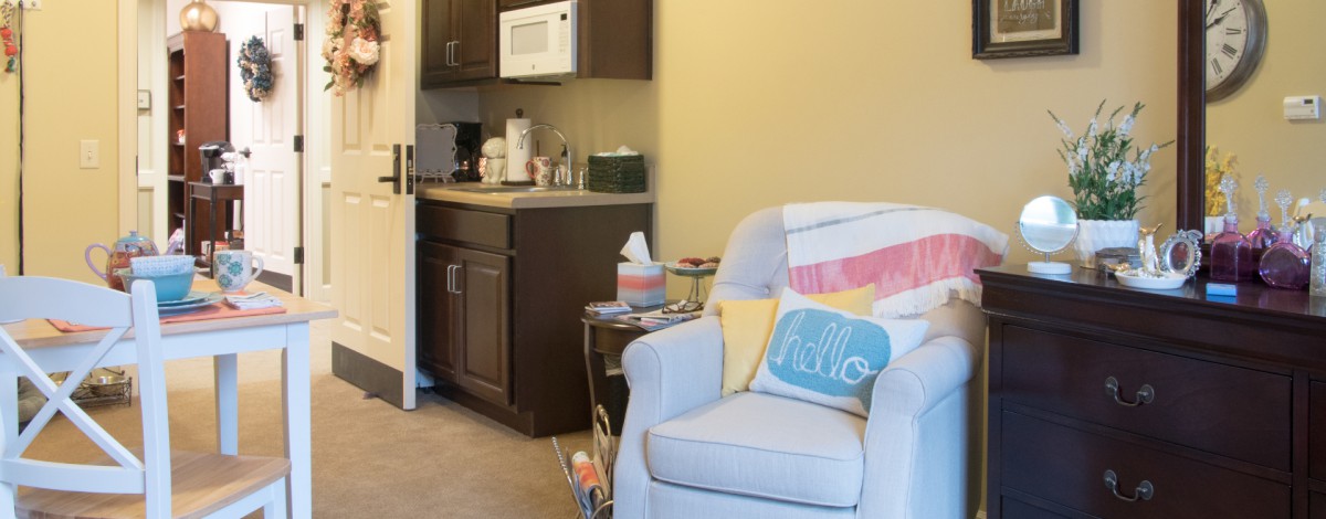 A cozy living space featuring an armchair with decorative pillows next to a kitchenette.