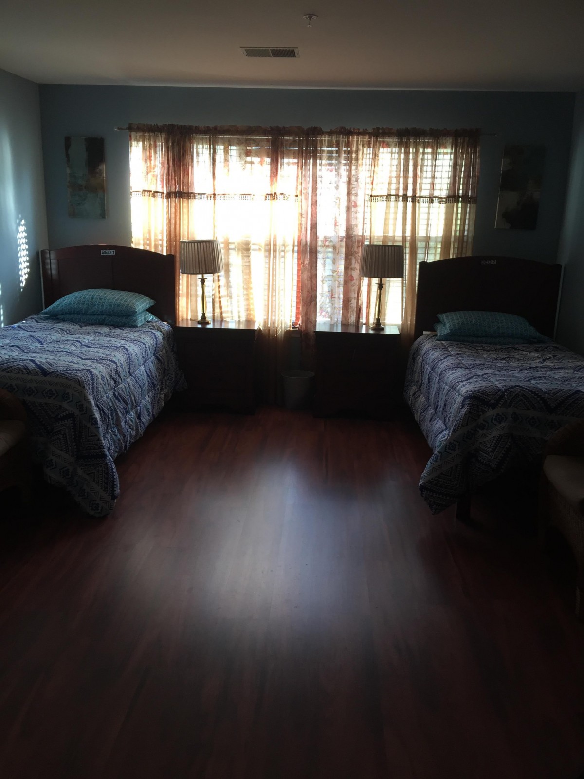 A cozy bedroom with two single beds and sunlight streaming through the window.